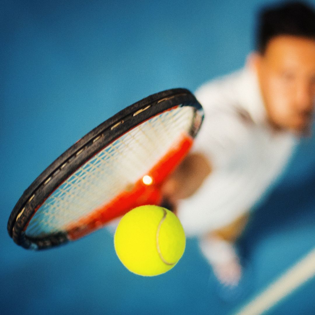 Tennis racket and ball in action with a player in the background