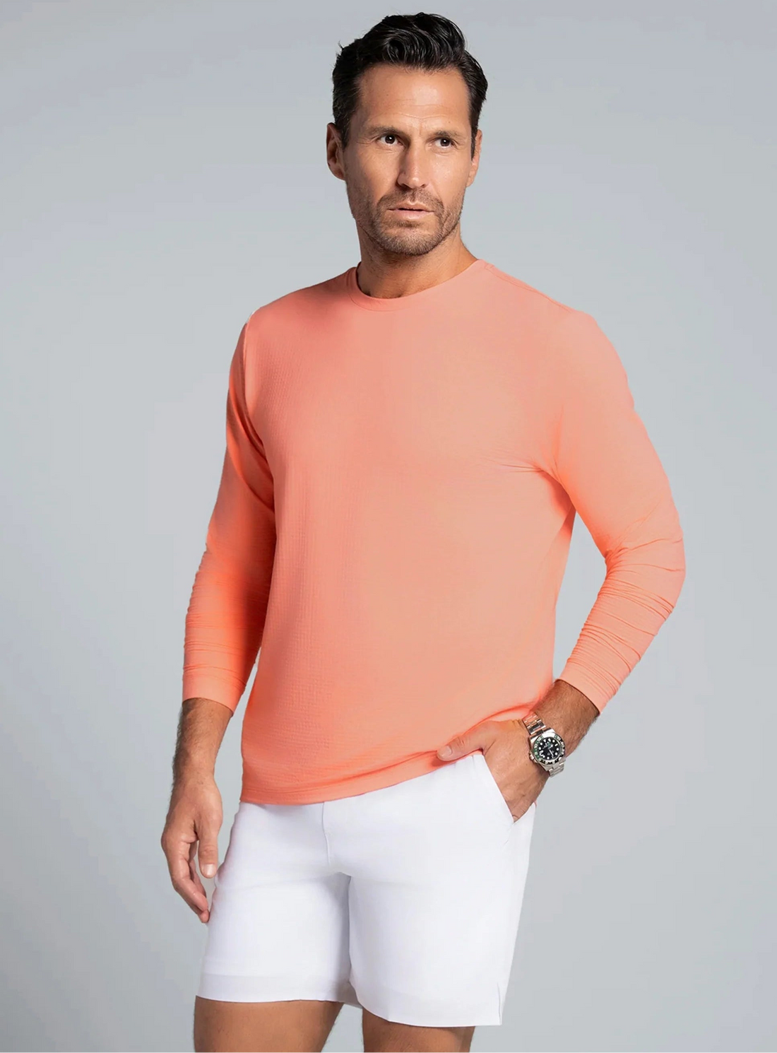 Man wearing a peach long-sleeve shirt and white shorts on a gray background