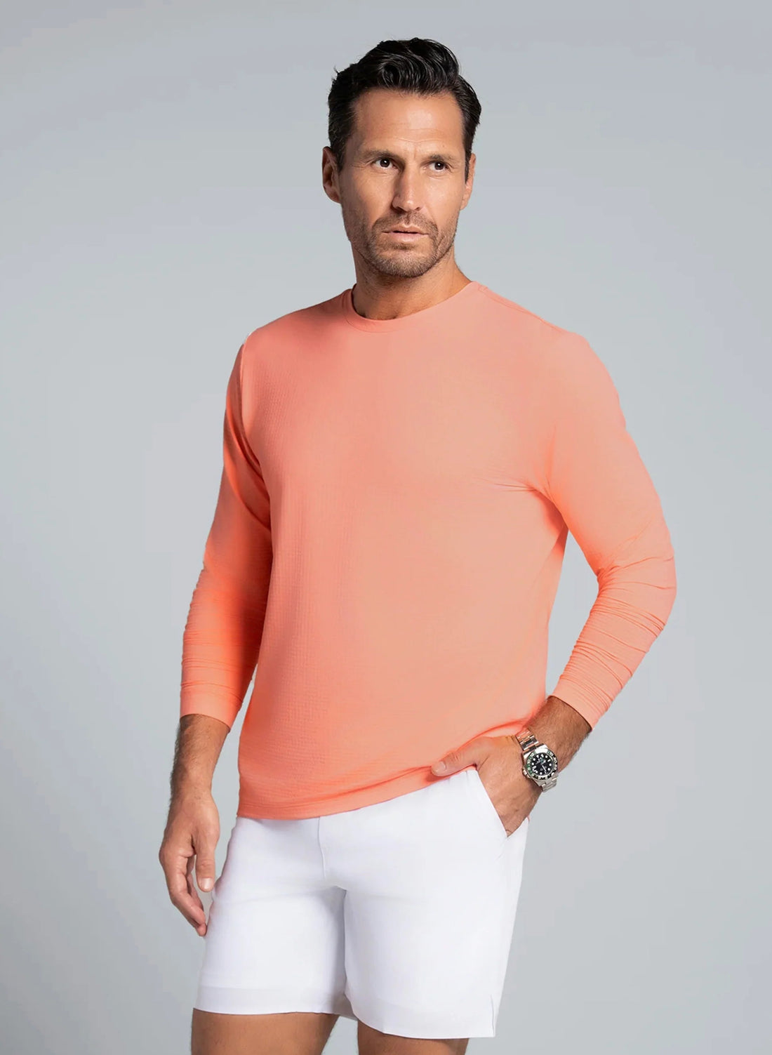 Man wearing a peach long-sleeve shirt and white shorts on a gray background