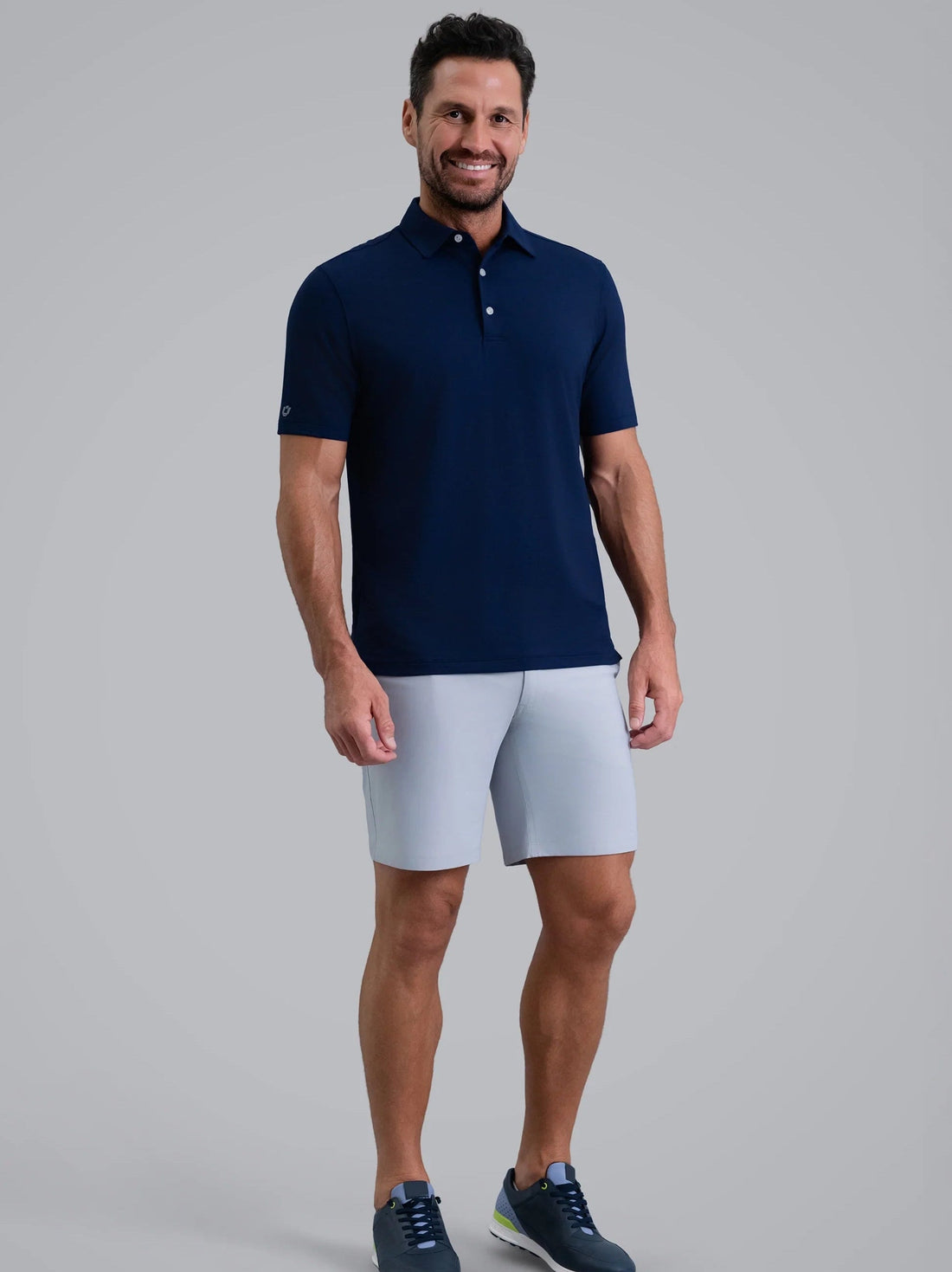 Man wearing a navy polo shirt and light gray shorts on a gray background