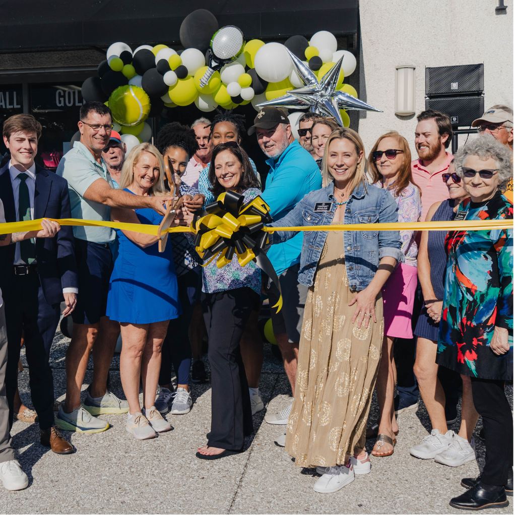 Group of people at a ribbon-cutting ceremony in front of a building with balloons and a star decoration.