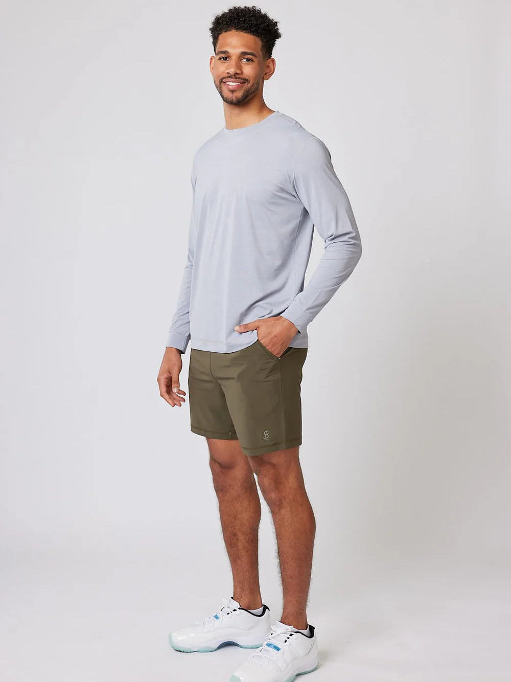 Man wearing a light gray long-sleeve shirt and green shorts on a white background