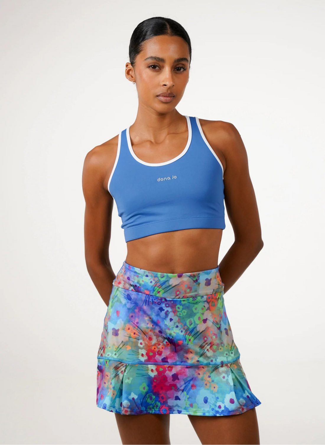 Woman wearing a blue sports bra and colorful tennis skirt on a white background