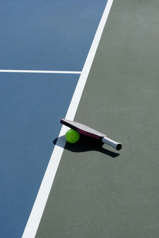 Pickleball paddle on top of a pickleball all on a sunny tennis court